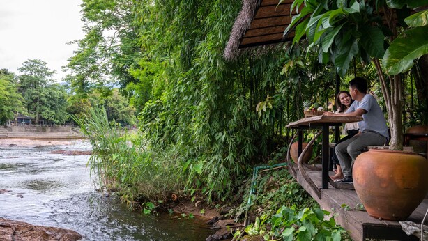 A wooden deck overlooking a river, with lush greenery and a thatched roof structure. - Phumontra Resort Nakhon Nayok (Nakhon Nayok)