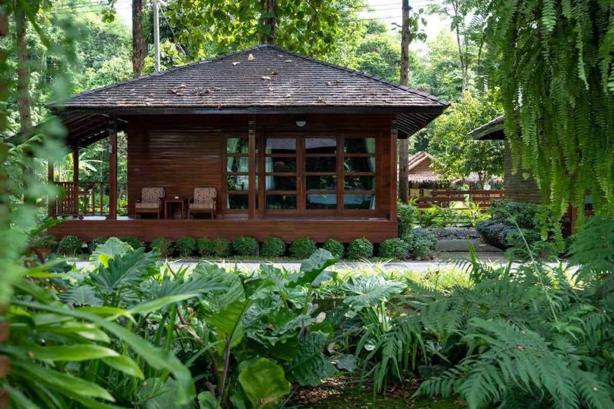 Una cabaña de madera con porche, ventanas amplias y rodeada de vegetación exuberante.