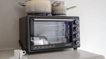 A compact kitchen with a built-in oven and microwave, a white cup on the counter, and two pots on top of the oven.