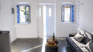 A spacious living area with a grey sofa, a coffee table with fruit, and a door leading to another room. - ArcadOia (Santorini)