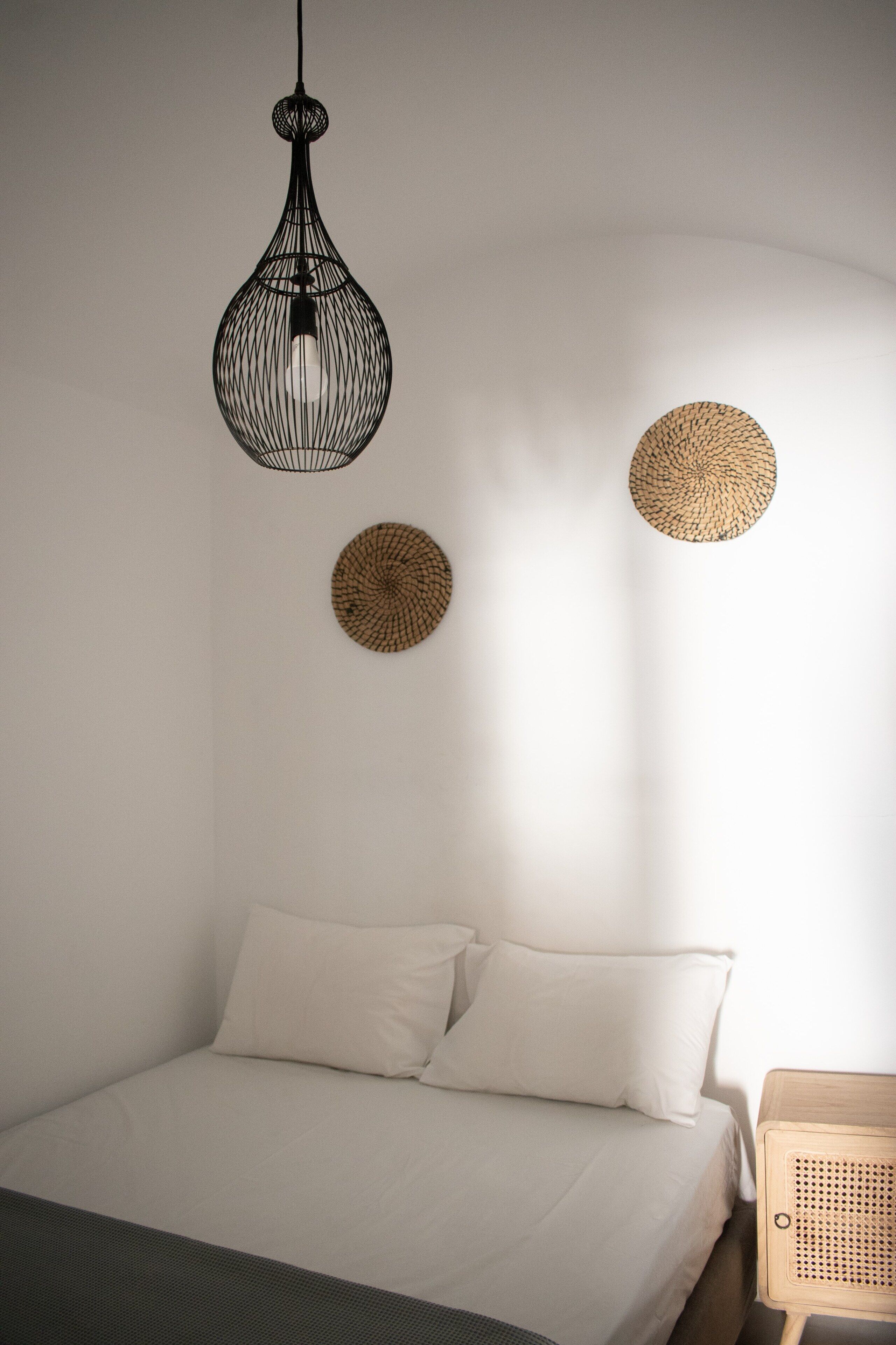 Un dormitorio con una cama, una lámpara colgante y dos elementos decorativos en la pared.