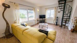A living room with a yellow sofa, a round coffee table, a TV, and a spiral staircase. - Villa near the beach with private pool (Calpe)