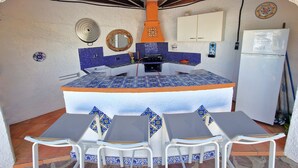 A compact kitchen with blue tiles, a white refrigerator, and a small dining area with white chairs. - Villa near the beach with private pool (Calpe)