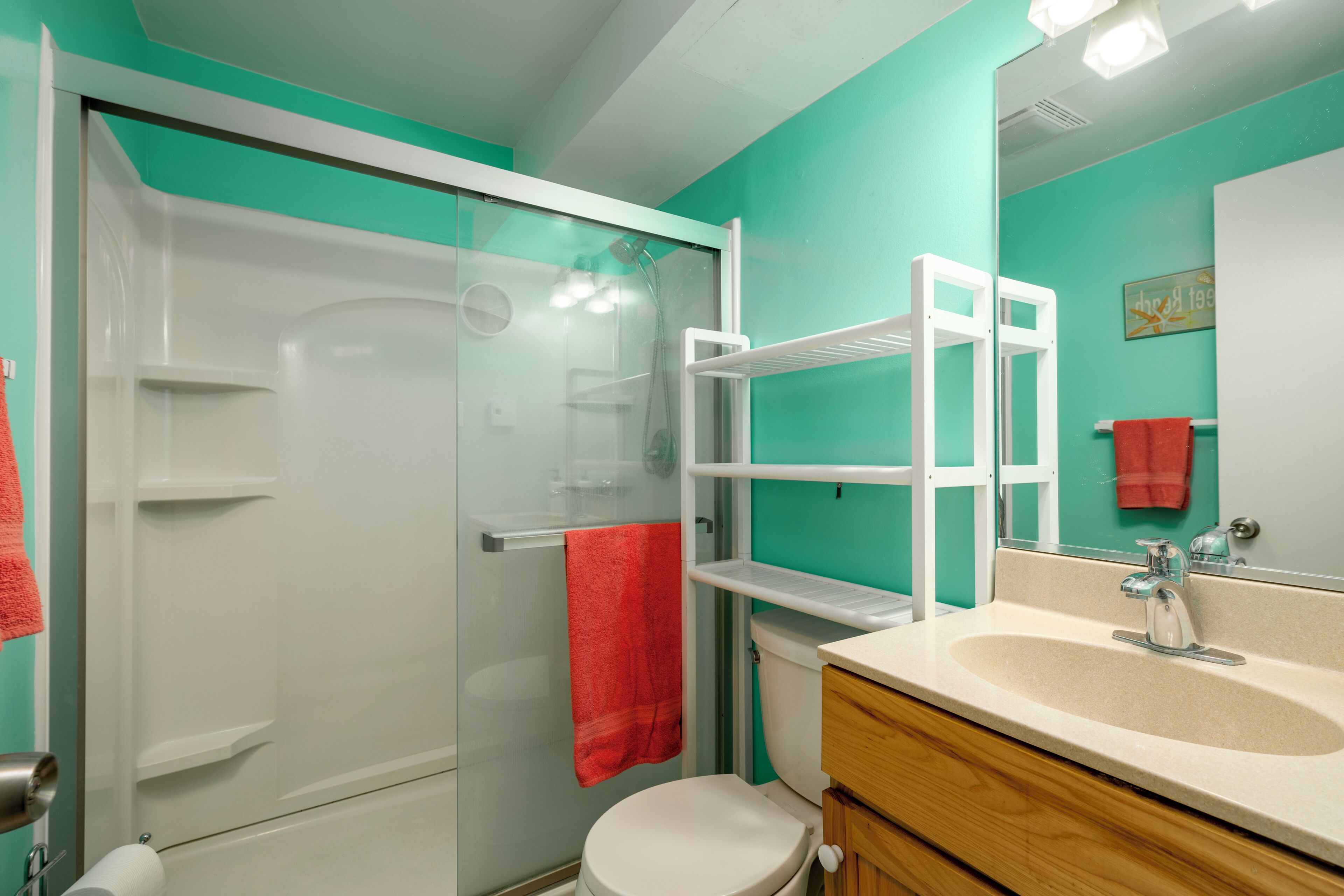 A bathroom with a glass shower enclosure, a white toilet, a sink with a mirror, and a red towel hanging on the wall.