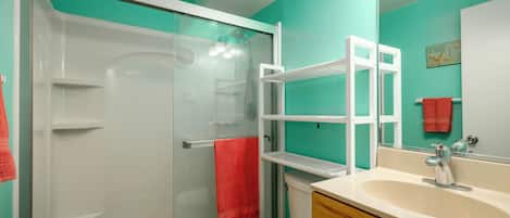 A bathroom with a glass shower enclosure, a white toilet, a sink with a mirror, and a red towel hanging on the wall.