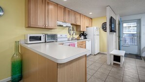 Una cocina con armarios de madera, una encimera blanca, microondas, tostadora, cafetera y refrigerador.