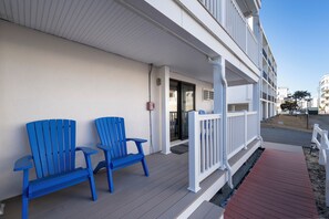 A building with a covered porch, two blue Adirondack chairs, and a white railing. - Cute ground floor condo, just 1/2 block to the beach (Ocean City)