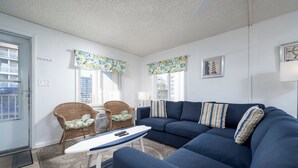 Una sala de estar con un sofá azul, dos sillones de mimbre, una mesita y cortinas estampadas.