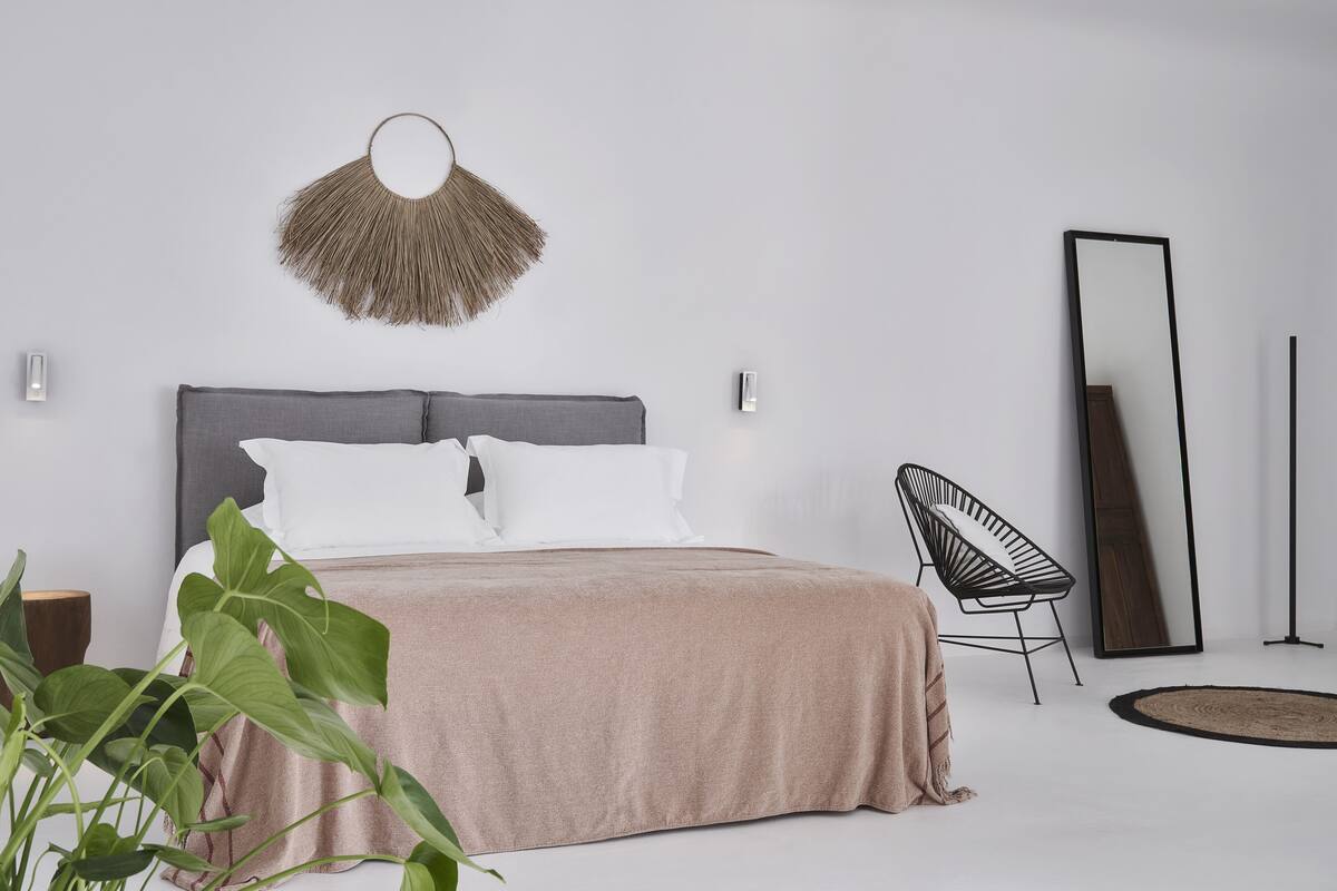 A modern bedroom with a bed, a chair, a large mirror, and a wall-mounted light fixture.