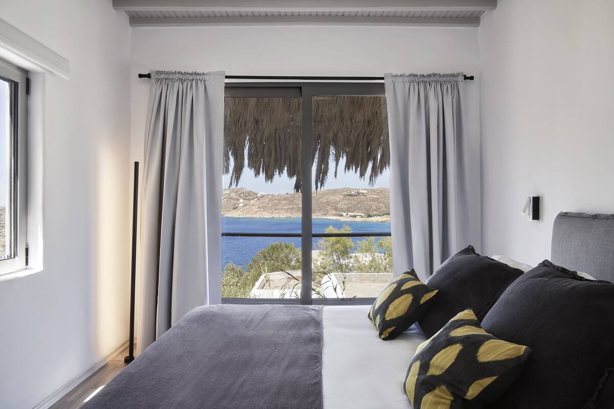 A bedroom with a large bed, a view of the sea, and a window with curtains.