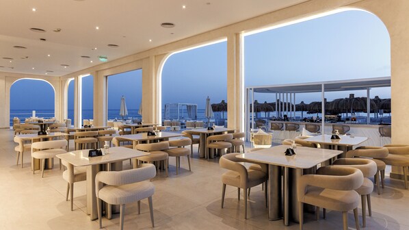 A spacious restaurant with large windows offering a view of the beach and ocean. Tables and chairs are arranged for dining. - SUNRISE Remal Beach Resort (Sharm El Sheikh)
