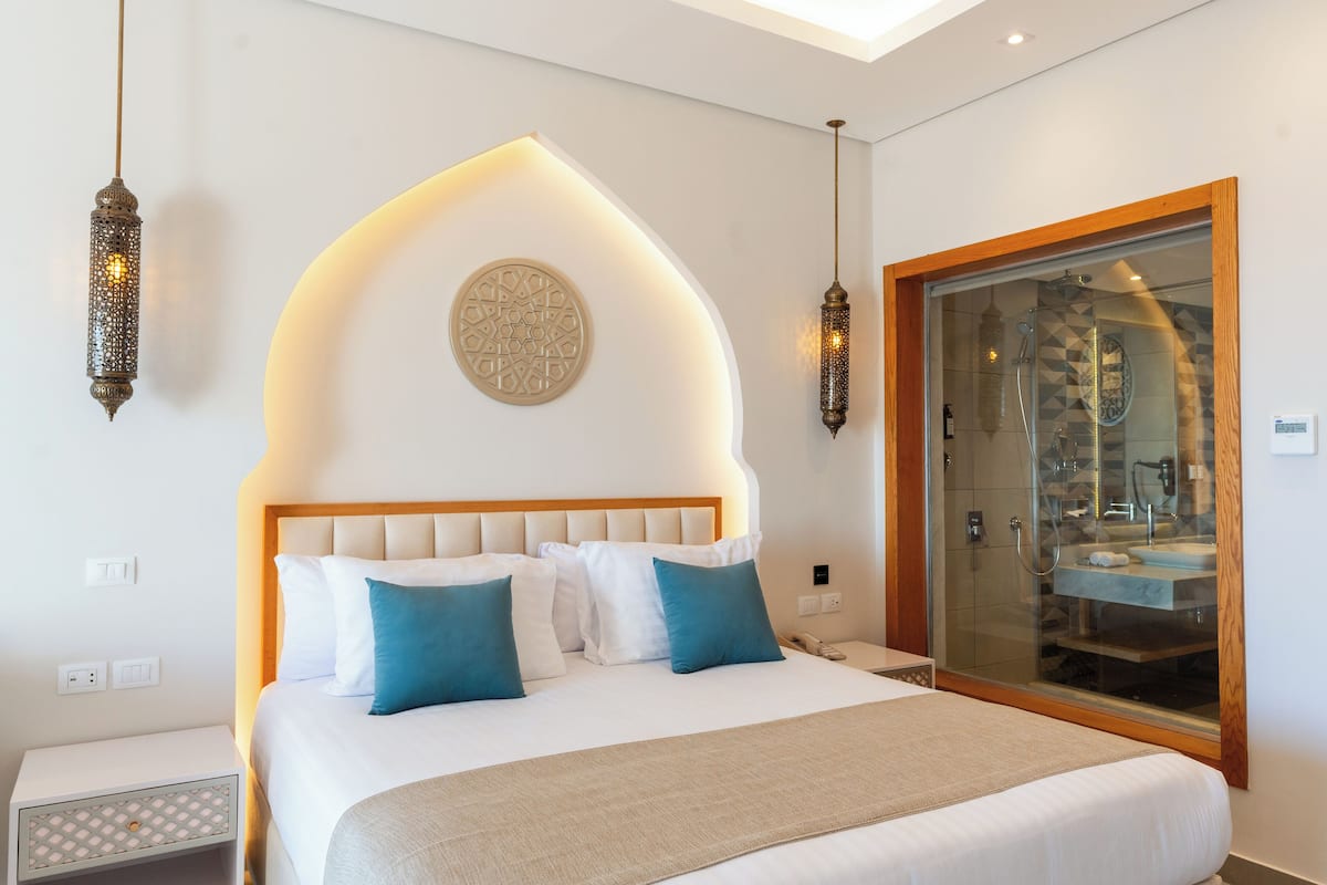 Ein modernes Hotelzimmer mit einem großen Bett, einer Duschkabine aus Glas und dekorativen Wandleuchten.