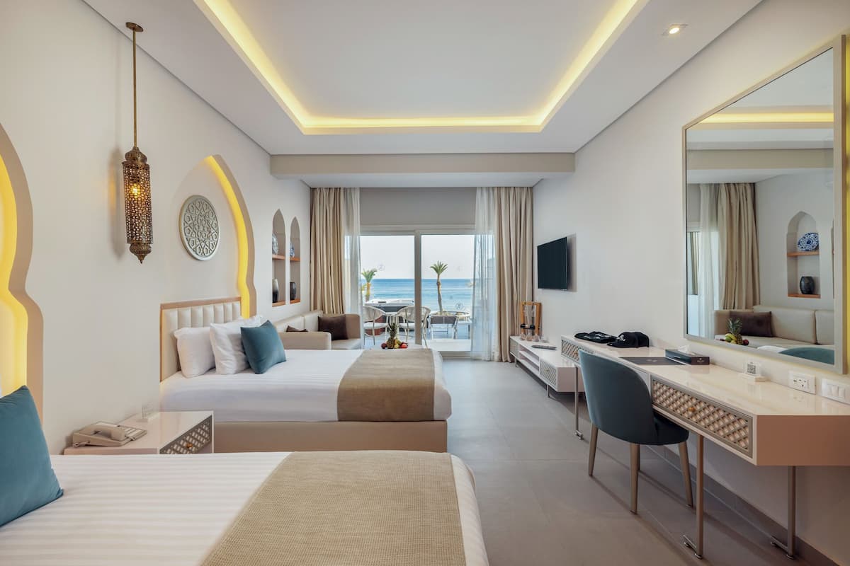 Ein Hotelzimmer mit zwei Betten, einem Schreibtisch, einem Sessel und Meerblick.