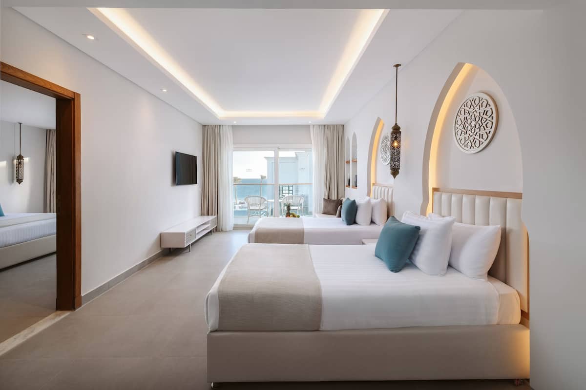 Ein Hotelzimmer mit zwei Betten, einem Fernseher, einem Balkon mit Blick und moderner Einrichtung.