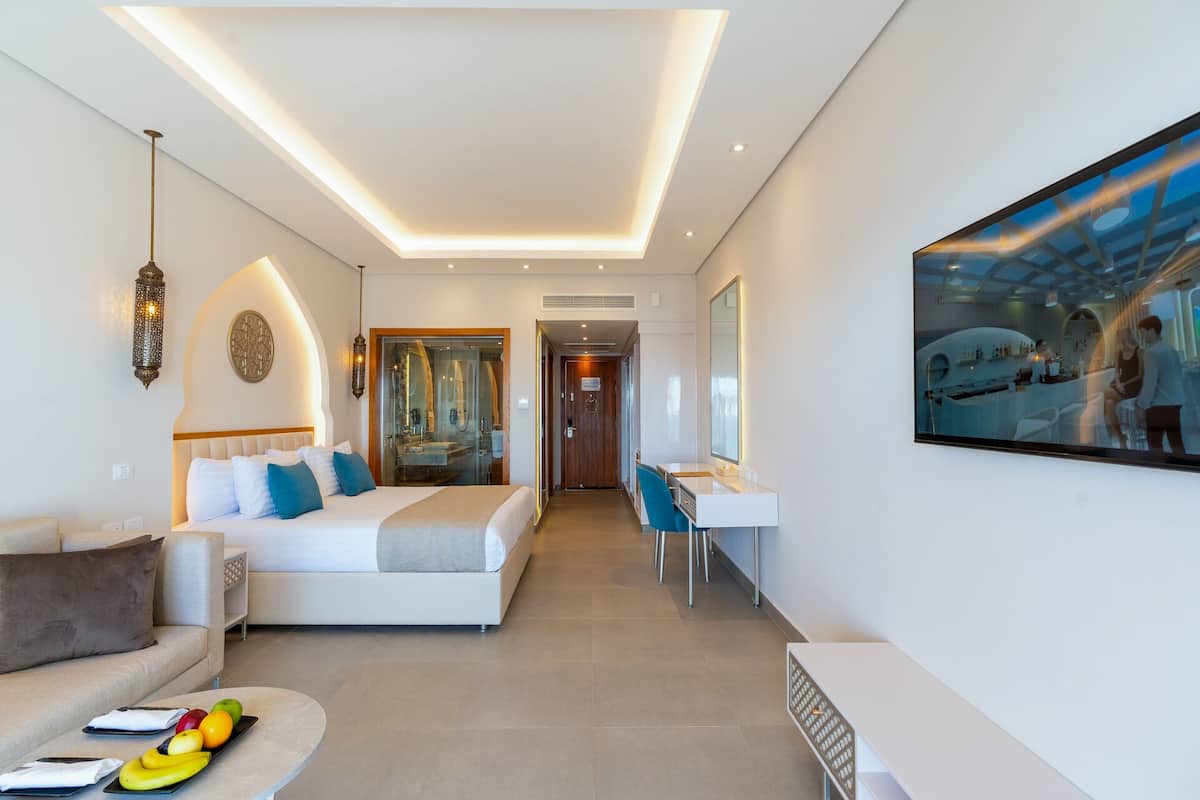 Ein modernes Hotelzimmer mit einem Bett, einer Sitzecke mit Sofa und Couchtisch, einem Schreibtisch mit Stuhl und einem großen Gemälde an der Wand.