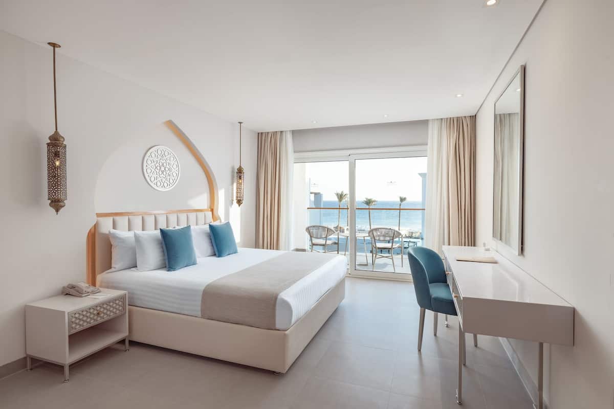 Ein modernes Hotelzimmer mit einem großen Bett, einem Schreibtisch und einem Balkon mit Meerblick.