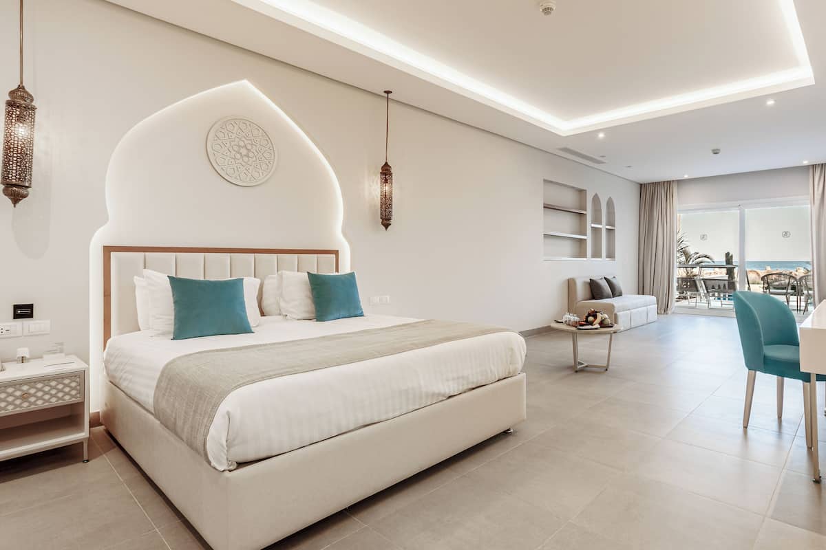 Ein modernes Hotelzimmer mit einem großen Bett, einer Sitzecke mit Tisch und Blick aufs Meer.