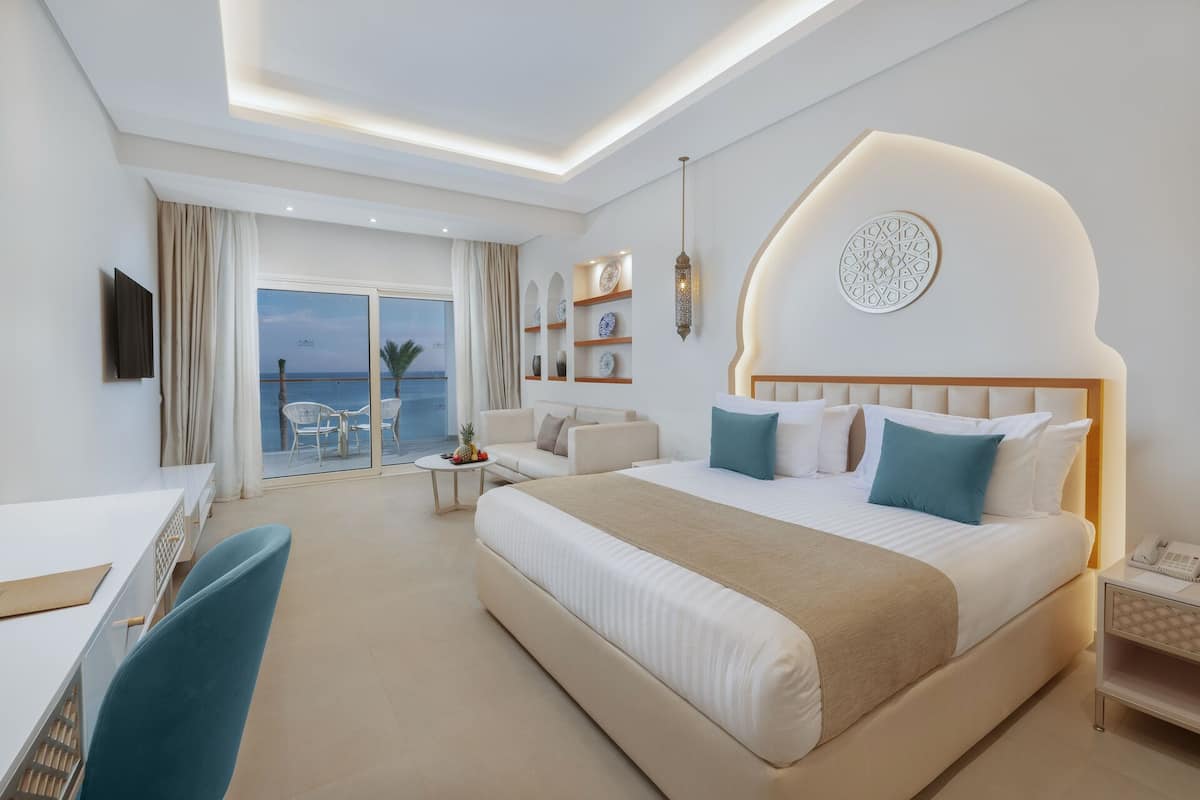 Ein modernes Hotelzimmer mit einem großen Bett, einem Schreibtisch und einem Balkon mit Meerblick.