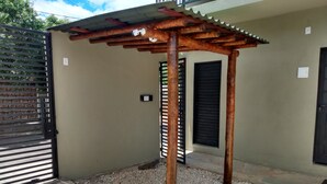 Un espace extérieur abrité doté d’une structure en forme de pergola, d’une entrée fermée par un portail et d’un sol en gravier.