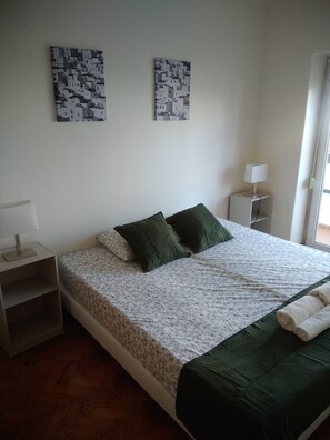 A bedroom with a bed, green pillows, a nightstand with a lamp, and two wall-mounted artworks.