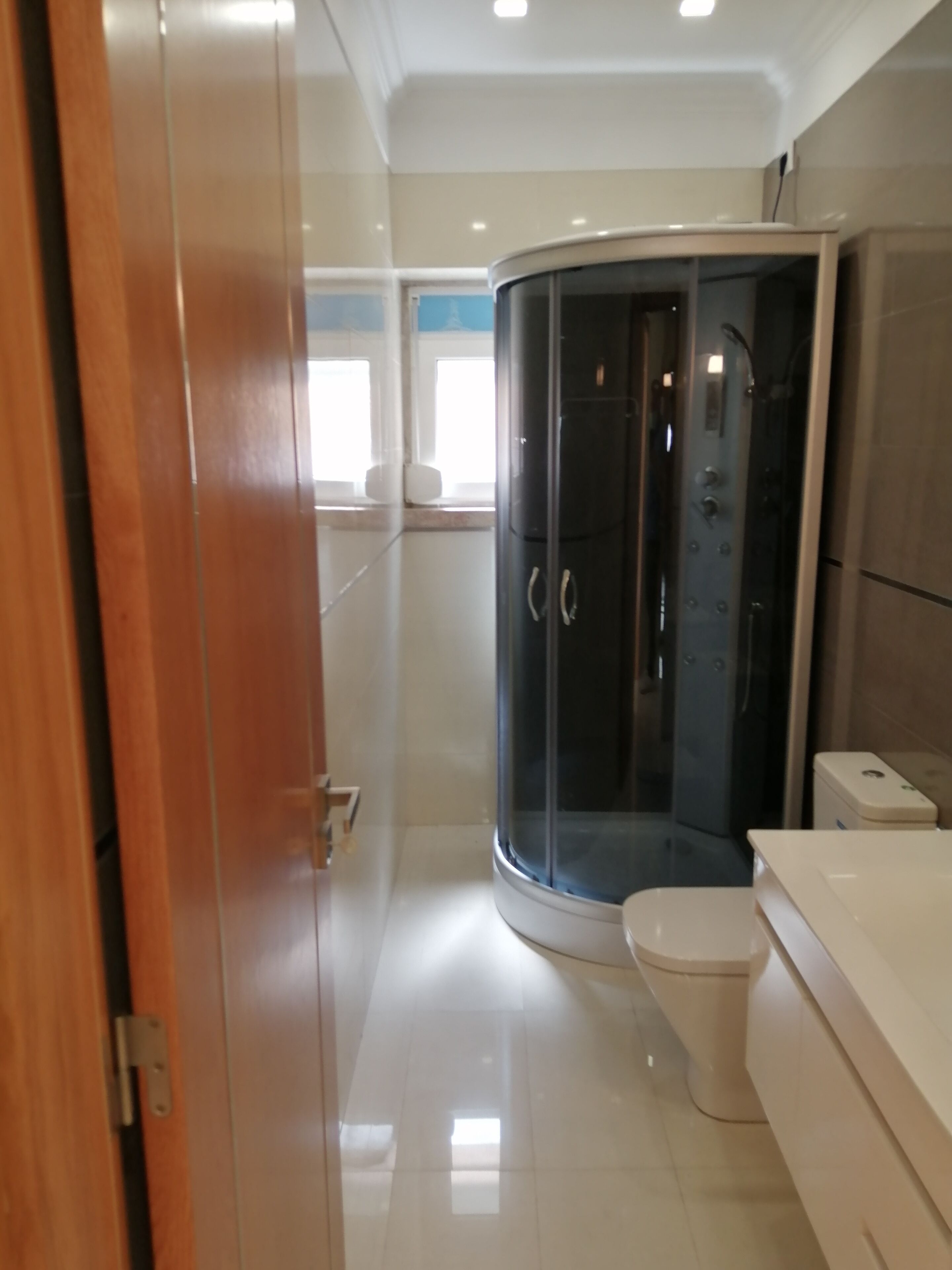 Een moderne badkamer met een douche in een glazen cabine, een toilet en een witte wastafel.