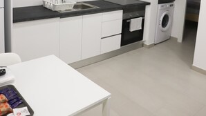 A modern kitchen with white cabinets, a black countertop, a sink, a stove, and a washing machine. - Oriente DNA Studios V (Loures)