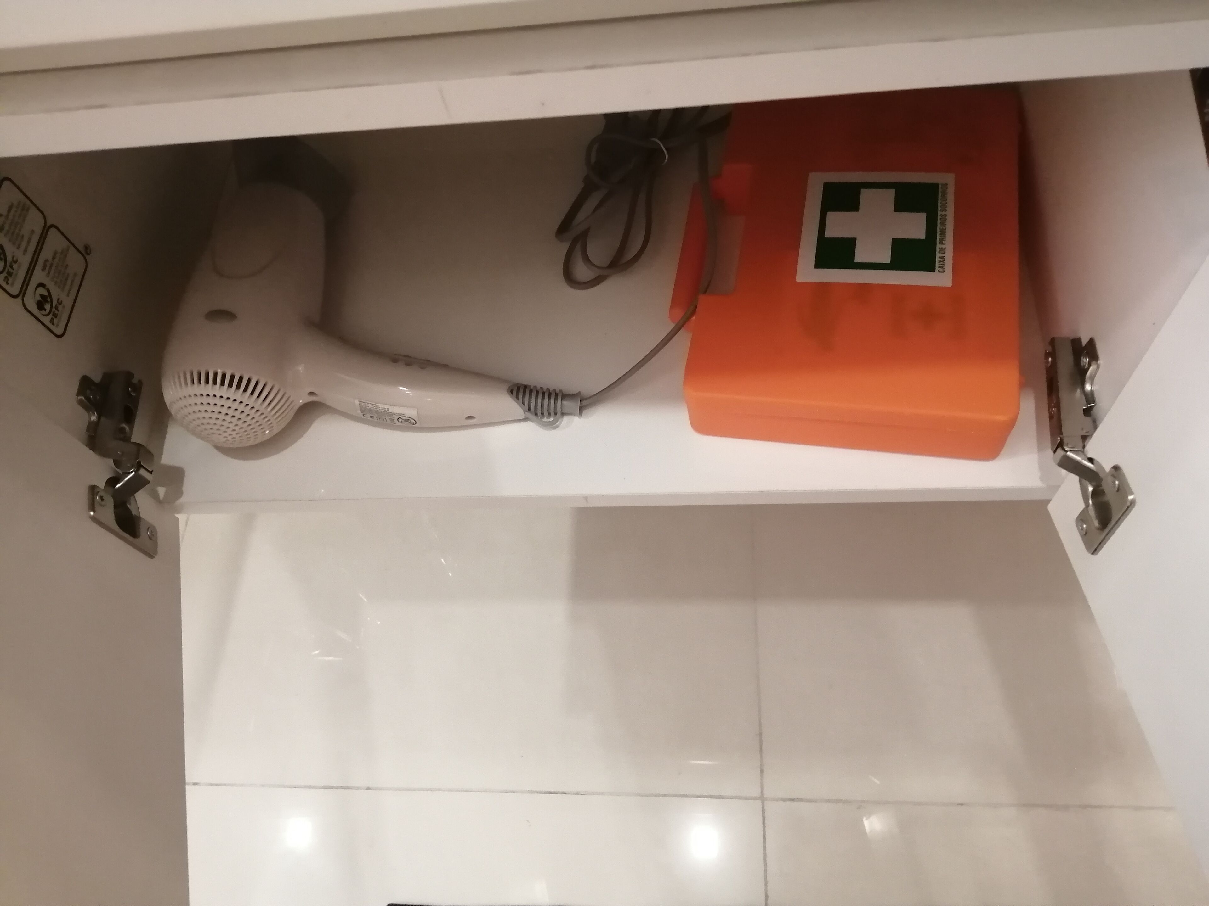 A bathroom with a white sink, a hairdryer, and an orange first aid kit.