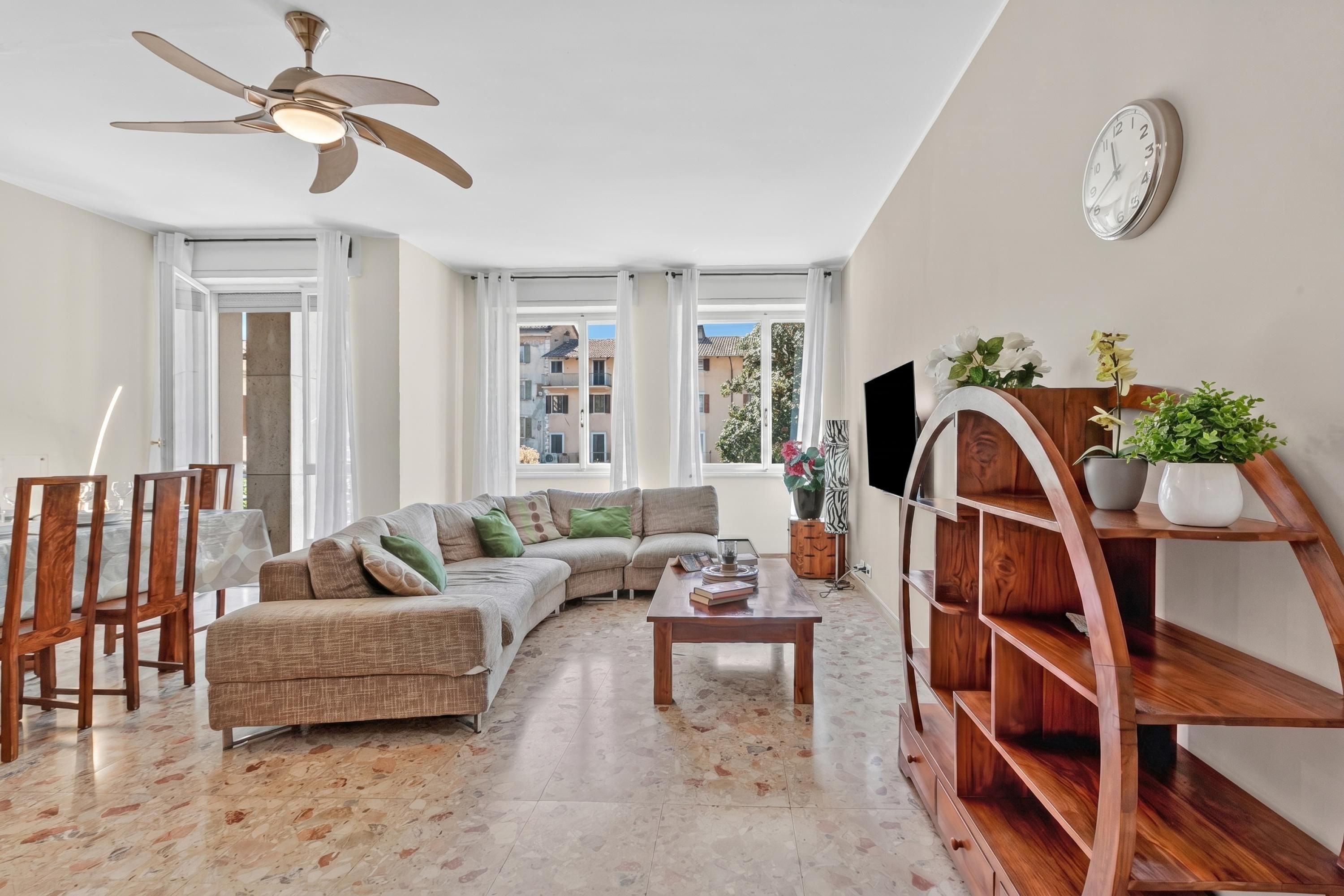 A living room with a sofa, coffee table, wooden bookshelf, TV, and large windows.
