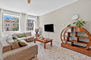 A living room with a sofa, coffee table, TV, and a wooden bookshelf. - Riva Dante Apartments (Riva del Garda)