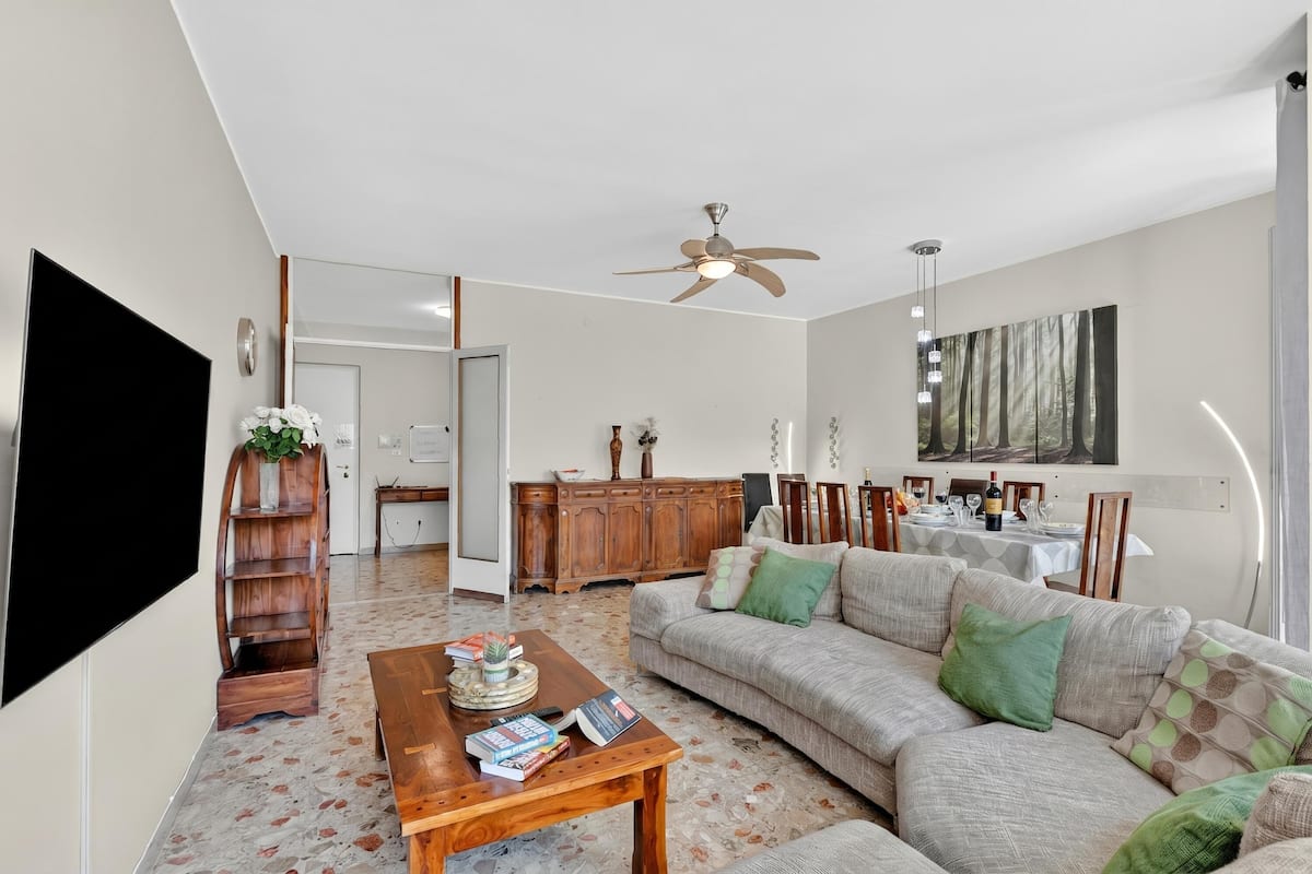 A living room with a sofa, coffee table, TV, and a dining area in the background.