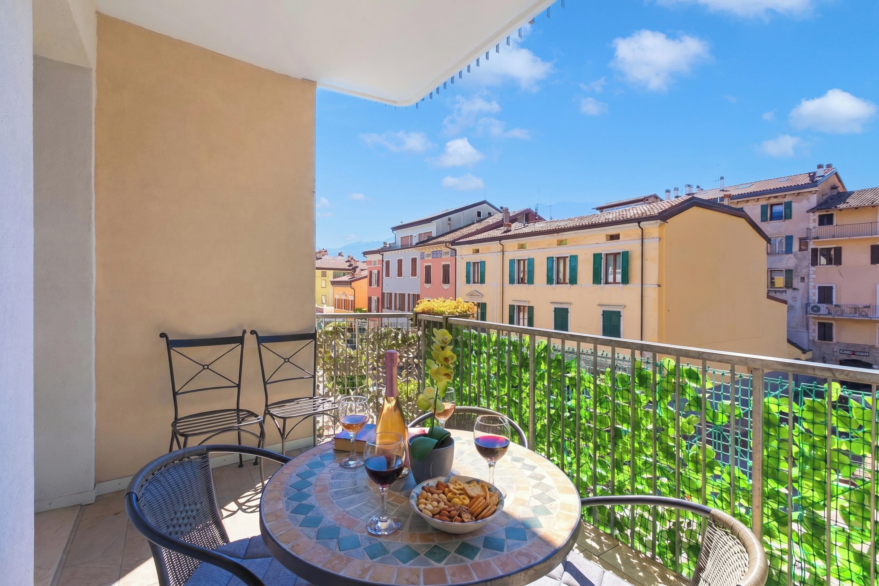 A balcony with a round table, chairs, a bottle, glasses, and snacks.