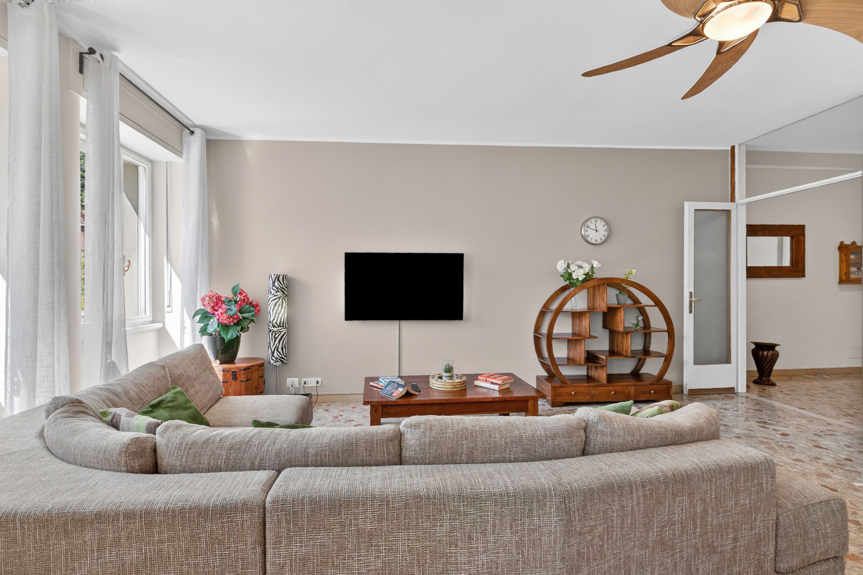 Un salon comprenant un canapé d’angle, une table basse en bois, un téléviseur à écran plat et un ventilateur de plafond.