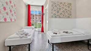 Une chambre d’hôtel avec deux lits, un luminaire au plafond, une porte donnant sur l’extérieur et un mur orné d’un motif floral.