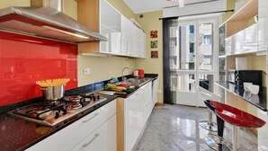 Une cuisine moderne avec une cuisinière à gaz, un pare-feu rouge, des armoires blanches et un tabouret de bar rouge.