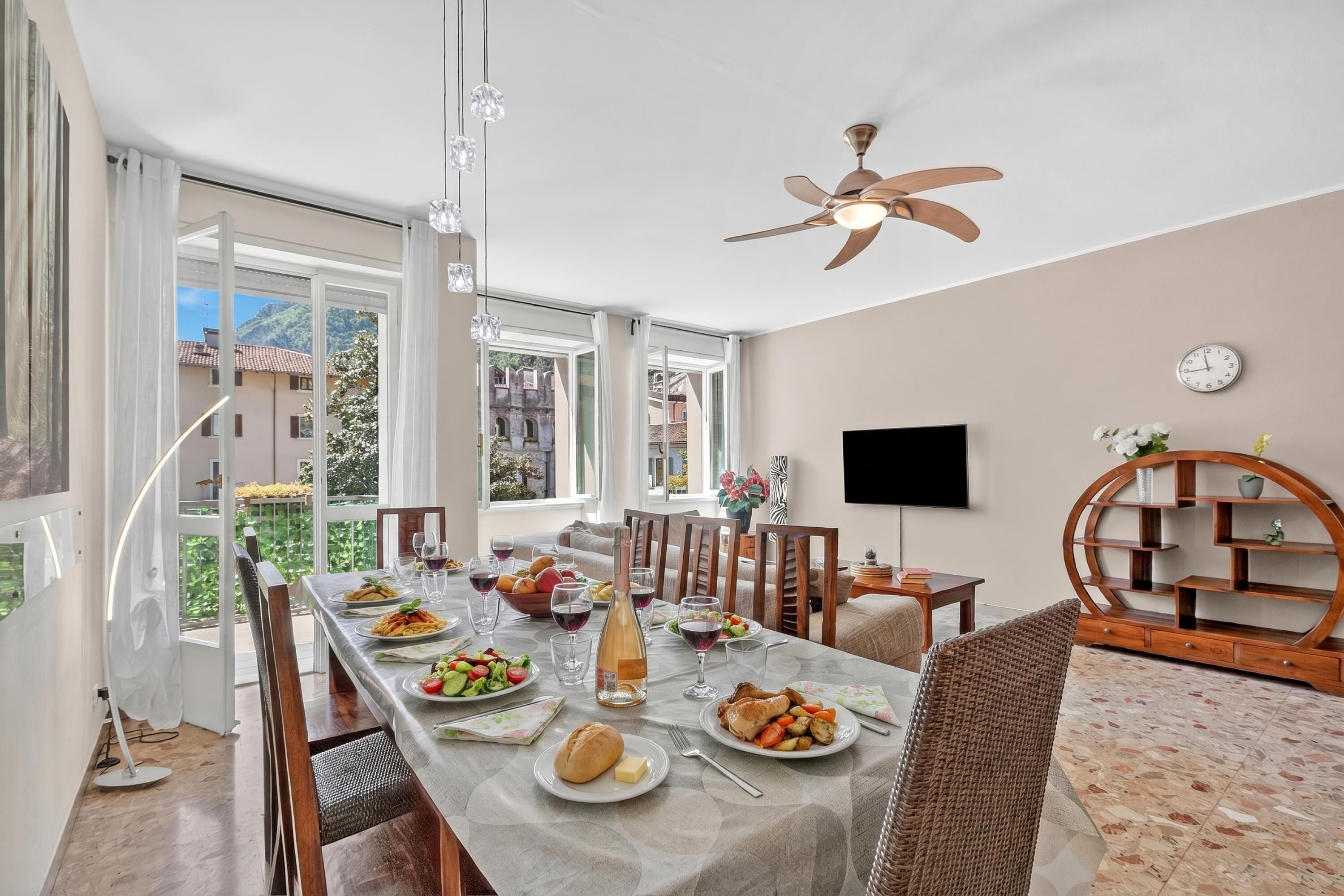 A dining area with a table set for a meal, a ceiling fan, and a view of the outside.