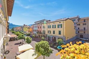 A street view with buildings, outdoor seating, and a clear sky. - Riva Dante Apartments (Riva del Garda)