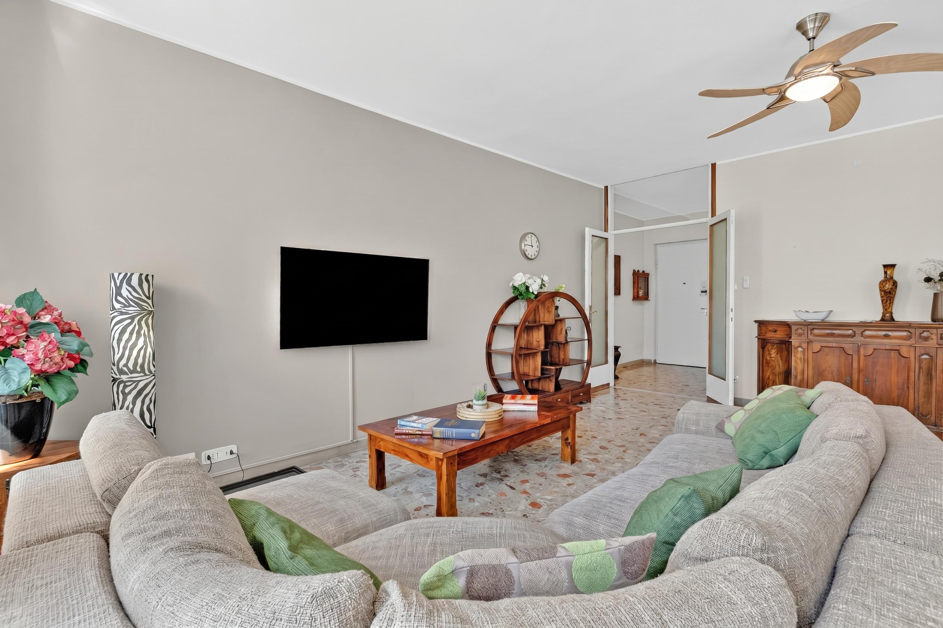 Una sala de estar con sofá, mesa de centro, televisor, ventilador de techo y un mueble de madera.