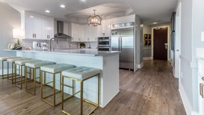 Una cocina moderna con armarios blancos, electrodomésticos de acero inoxidable y una isla central con taburetes de bar.
