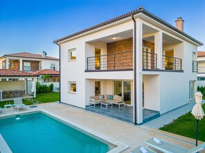 Ein modernes, zweistöckiges Haus mit Swimmingpool, Sitzgelegenheiten im Freien und einem gepflegten Garten.