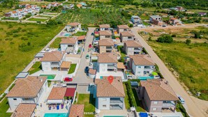 Vue aérienne d’un quartier résidentiel composé de nombreuses maisons à deux étages, chacune dotée d’un toit en tuiles et d’une piscine.