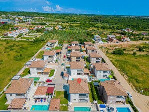 An aerial view of a residential area with multiple two-story houses, each featuring a tiled roof and a swimming pool.