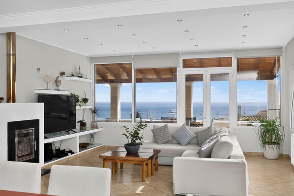 A modern living room with a fireplace, a sofa, a coffee table, and a view of the sea.