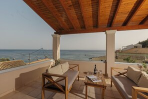 A covered outdoor seating area with a view of the sea, featuring a wooden table and two sofas.