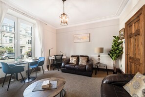 A modern living room with a leather sofa, a dining table with chairs, a standing lamp, and a large window with curtains. - Cozy West End Aberdeen 1 Bed Flat Easy Access (Aberdeen)