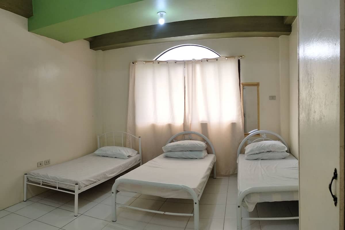 Ein Zimmer mit drei Einzelbetten, einem Fenster mit Vorhängen und einer Tür.