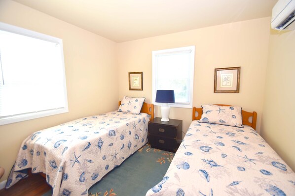 A bedroom with two single beds, a nightstand, a lamp, and framed pictures on the wall.