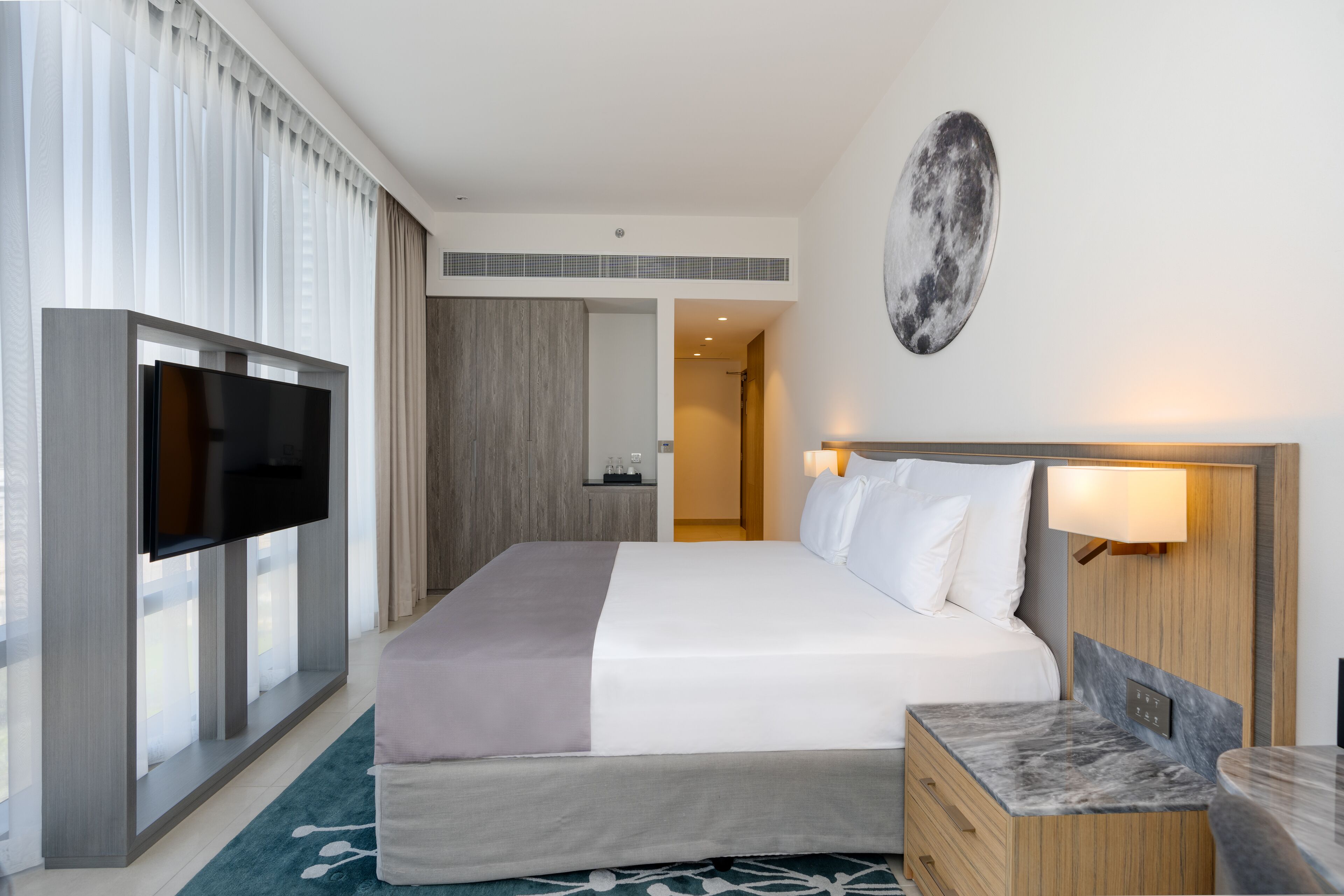 Een moderne hotelkamer met een groot bed, een flatscreen televisie, een marmeren nachtkastje en een wandlamp.