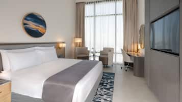 Quarto de hotel com uma cama grande, uma escrivaninha com cadeira, uma televisão e uma janela com cortinas.