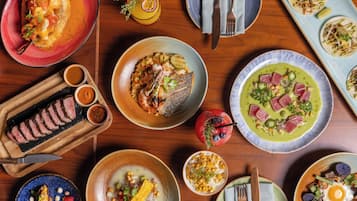 Diversos pratos sobre uma mesa de madeira, incluindo peixe, tacos e uma tigela de milho.