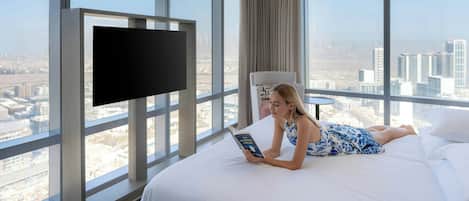 Habitación de hotel con una cama grande, un televisor de pantalla plana montado en la pared y vistas a la ciudad a través de amplias ventanas.